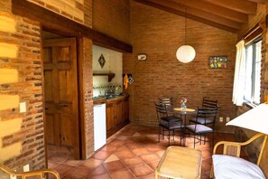 A rustic kitchen with a brick wall, wooden cabinets, and a dining area with a table and chairs. - Scenic Cabin Retreat in Breathtaking Tepoztlán (Tepoztlán)