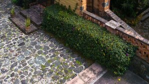 A rustic house with a sloped roof, surrounded by lush greenery and hills.