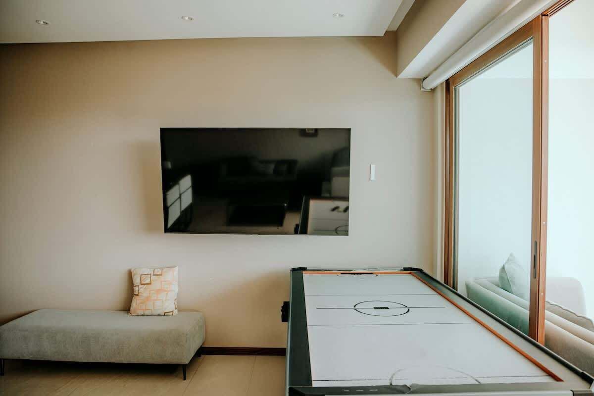 Une pièce dotée d’un téléviseur à écran plat fixé au mur, d’une table de billard, d’un canapé et d’une grande fenêtre.