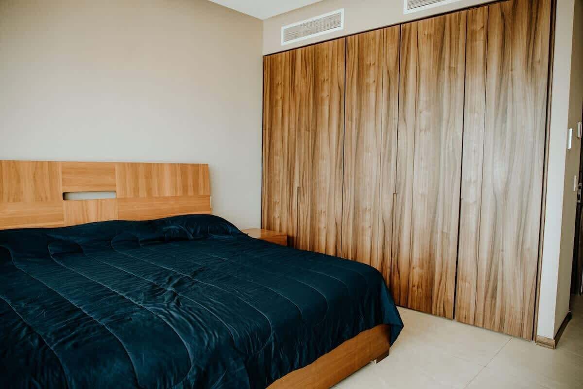 Une chambre à coucher avec une tête de lit en bois, un grand lit recouvert d’une couvre-lit bleu foncé et une armoire en bois.