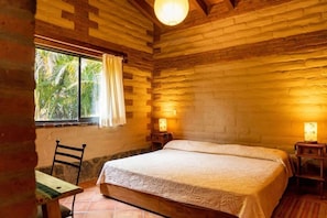 Ein Zimmer mit Bett, Stuhl, Tisch und einem Fenster mit Vorhängen.