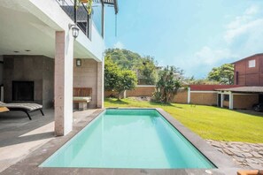 Una piscina con bordo in pietra, un'area salotto coperta e vista su una collina.
