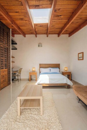 Una camera da letto con finestra a lucernario, un letto, comodini, una sedia, un divano e un armadio in legno.