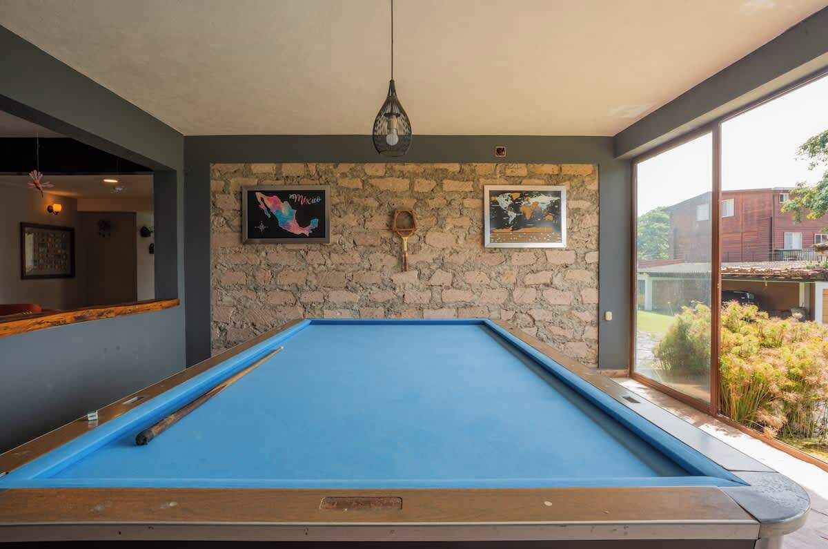 Een pooltafel met een achtergrond van een stenen muur, kunstwerken, een hangende lamp en een uitzicht op een gebouw door een glazen deur.