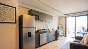 A modern kitchen with stainless steel appliances, a dishwasher, and a large window. - Chic Roma Norte Studio w/ Private Balcony (Mexico City)