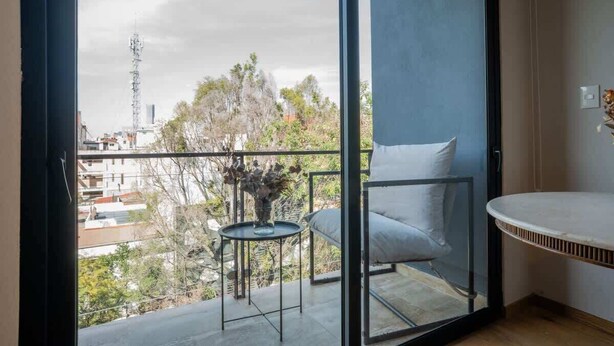 A balcony with a view of the city, a small table with a vase, and a chair. - Chic Roma Norte Studio w/ Private Balcony (Mexico City)
