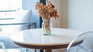 A round dining table with a vase of dried flowers, clear chairs, and a view of the outdoors through a window. - Chic Roma Norte Studio w/ Private Balcony (Mexico City)