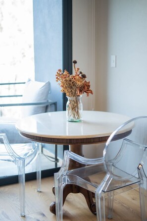 A round dining table with a vase of dried flowers, clear chairs, and a view of the outdoors through a window. - Chic Roma Norte Studio w/ Private Balcony (Mexico City)