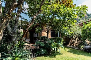 A house with a brick exterior, surrounded by lush greenery and a well-maintained lawn. - Charming Cabin Retreat in Magical Tepoztlán (Tepoztlán)