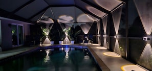 A modern indoor pool area with geometric ceiling design, lounge chairs, and potted plants. - Paradise Skye Golf, Pool & Beach Retreat (Rotonda West)