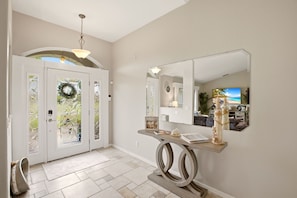 A foyer with a double door, a mirror, a console table with decorative items, and a tiled floor. - Paradise Skye Golf, Pool & Beach Retreat (Rotonda West)
