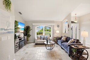 A living room with a sofa, coffee table, and a view through a window. - Paradise Skye Golf, Pool & Beach Retreat (Rotonda West)