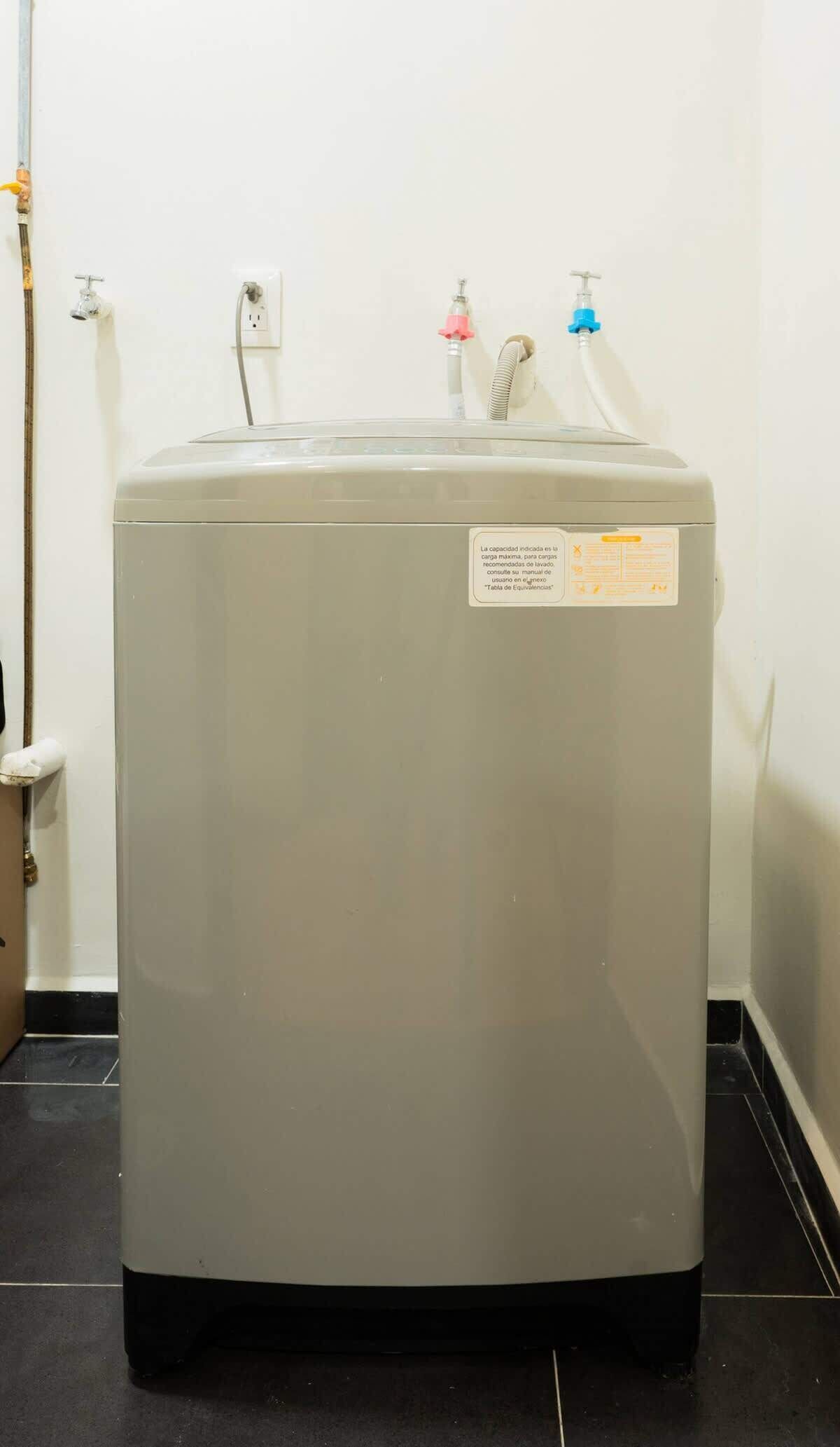 A gray water heater with a label, a faucet, and a power outlet on the wall.