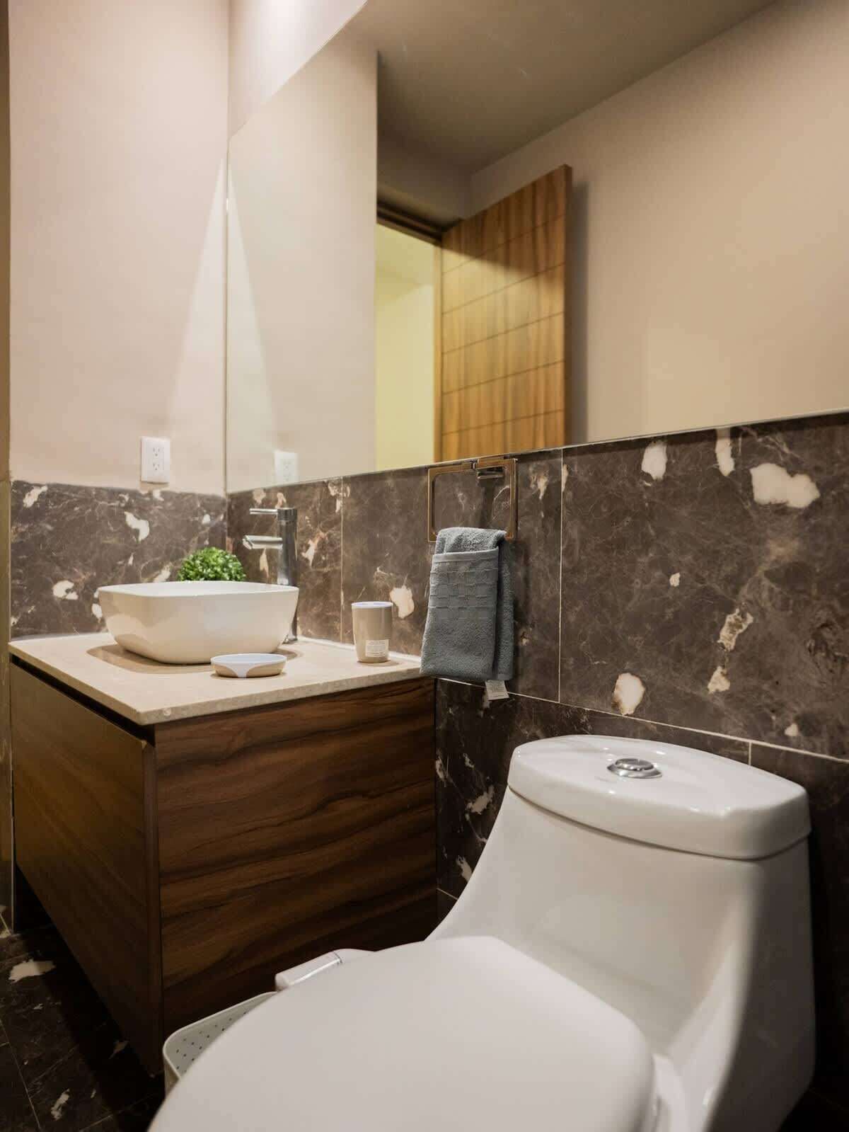 A modern bathroom with a marble vanity, a toilet, and a mirror.