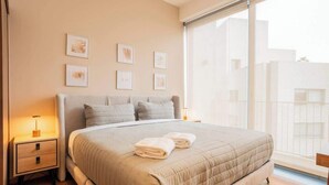 Een slaapkamer met een groot bed, nachtkastjes, afbeeldingen in lijsten aan de muur en een raam met uitzicht.