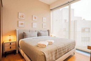 Ein Schlafzimmer mit einem großen Bett, Nachttischen, gerahmten Bildern an der Wand und einem Fenster mit Blick.