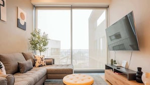 Een moderne woonkamer met een bank, poef, televisie en een plant.