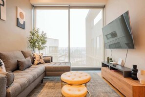 Ein modernes Wohnzimmer mit einer Couch, Hocker, Fernseher und einer Pflanze.