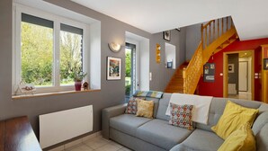 Un salon avec un canapé gris, un escalier en bois et une fenêtre donnant sur un paysage verdoyant.