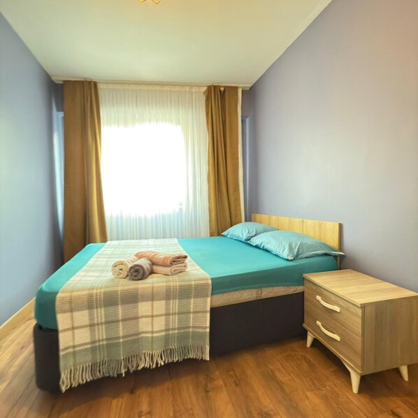 A bedroom with a bed, a bedside table, and a window with curtains. - Aras Suit (Bursa)