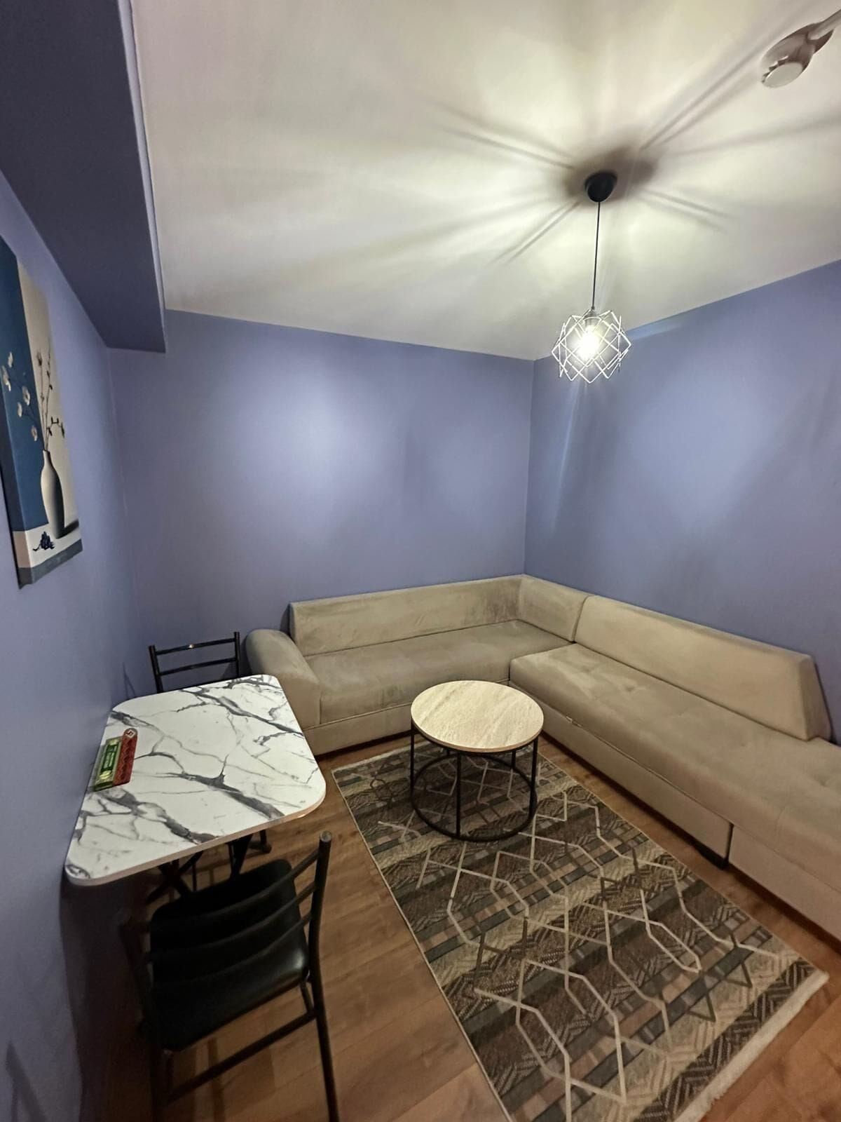 A room with a marble table, a beige sofa, a patterned rug, and a hanging light fixture.