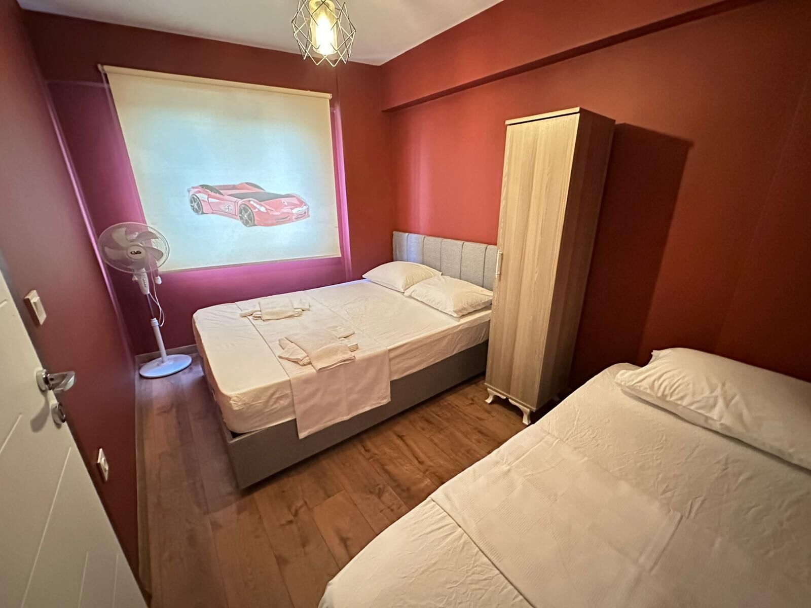 A bedroom with a bed, a wardrobe, a fan, and a wall-mounted projector displaying a car.