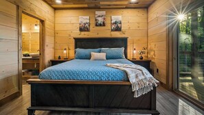 Ein Schlafzimmer mit Holzwandverkleidung, einem Bett, Nachttischen und Blick durch ein großes Fenster.