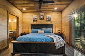 A wooden-paneled bedroom with a bed, bedside tables, and a view through a large window. - Lexy Lane Indoor Pool | Mountain Views | Sleeps 12 (Sevierville)