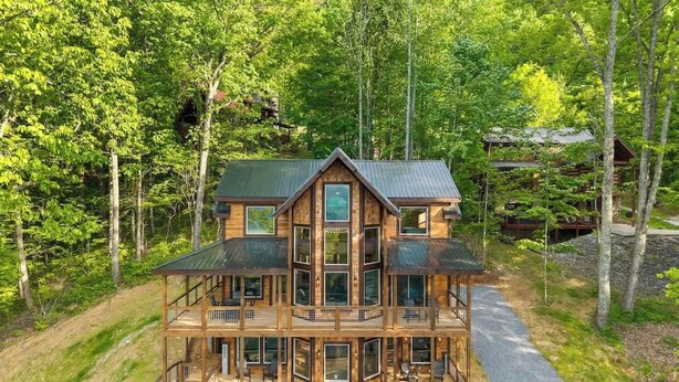 Eine mehrstöckige Holzhütte mit einem Balkon, umgeben von dichtem Wald.