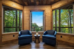 A room with wooden walls and large windows, two blue chairs, and a small table with a vase. - 4-Bedroom Sevierville Cabin with Indoor Pool, Hot Tub & Game Room (Sevierville)