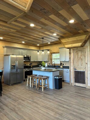 A modern kitchen with wooden beams, stainless steel appliances, and a central island with stools. - Lexy Lane Indoor Pool | Mountain Views | Sleeps 12 (Sevierville)