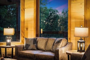A cozy room with a leather sofa, two side tables with lamps, and a view of trees through large windows. - Lexy Lane Indoor Pool | Mountain Views | Sleeps 12 (Sevierville)