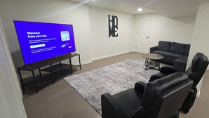 Olohuoneessa on litteänäyttöinen televisio, harmaa sohva, pieni pyöreä pöytä ja harmaa matto.
