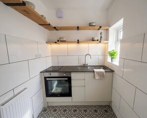 Eine kleine Küche mit weißen Fliesen, einer schwarzen Arbeitsplatte, einem eingebauten Backofen und einem Fenster mit einer Pflanze.