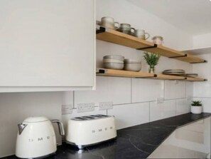 Eine Küche mit weißen Schränken, einer schwarzen Arbeitsplatte, einem weißen Toaster und einem weißen Wasserkocher.