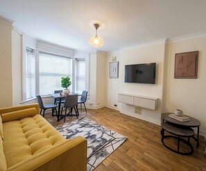 Ein Wohnzimmer mit einer Couch, einem Esstisch, Stühlen, einem Fernseher und Kunstwerken an den Wänden.