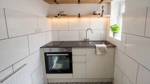 Ett kompakt kök med vita skåp, en svart bänkskiva, en inbyggd ugn och ett fönster med en växt.