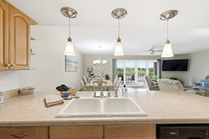 A kitchen with a double sink, wooden cabinets, pendant lights, a dining area with a table and chairs, and a TV mounted on the wall. - Holiday Villas 2 Unit 206 (Indian Shores)