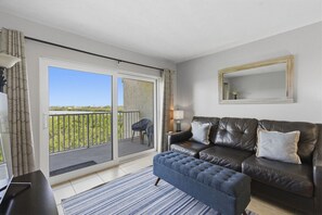 Un saló amb un sofà, una taula de centre, una làmpada i vista a un balcó amb cadires.