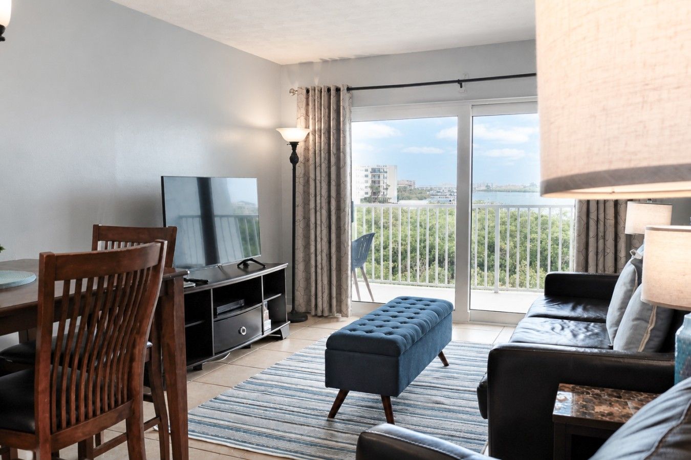 Ein modernes Wohnzimmer mit Fernseher, Esstisch mit Stühlen, einer Couch und einem Balkon mit Aussicht.