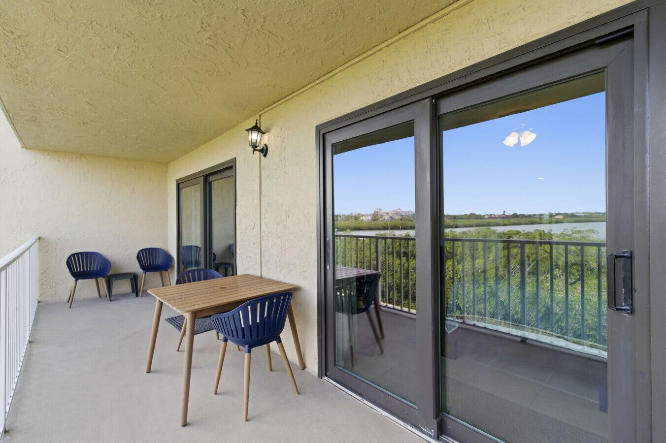 Un balcon avec une table et des chaises, une porte-fenêtre coulissante et une vue sur une rivière et la verdure.