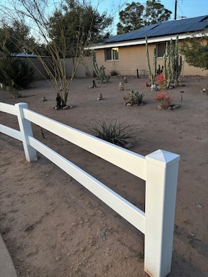 A fenced outdoor area with cacti and a building with solar panels. - A Cozy One-Person Studio (Mesa)
