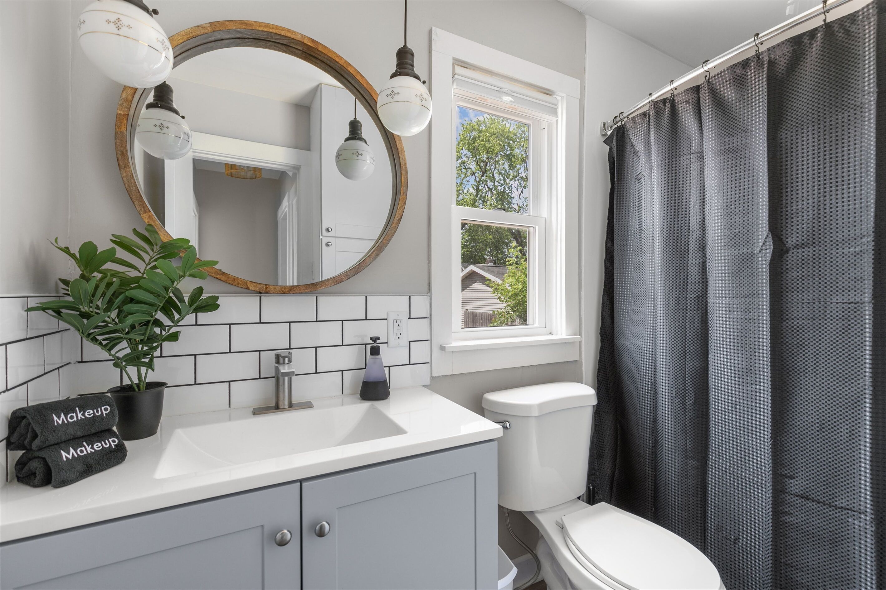 A bathroom with a white sink, a mirror with a wooden frame, a potted plant, and a shower curtain.