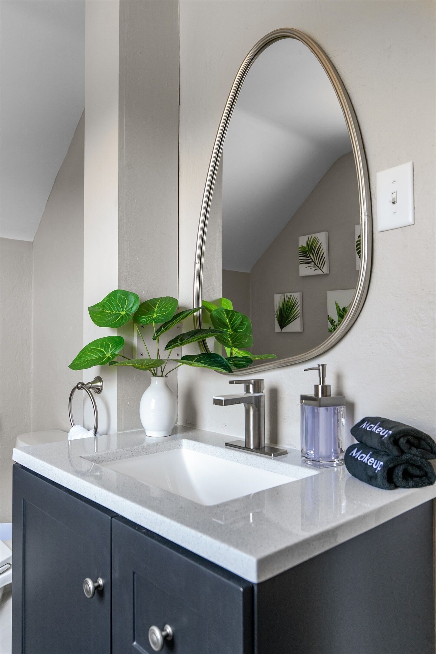 Une salle de bain avec un lavabo blanc, un grand miroir, une plante en pot et une serviette.