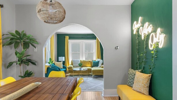 Una sala de estar moderna con una mesa de comedor de madera, sillas amarillas, una pared de acento verde y vistas al área de comedor contigua.