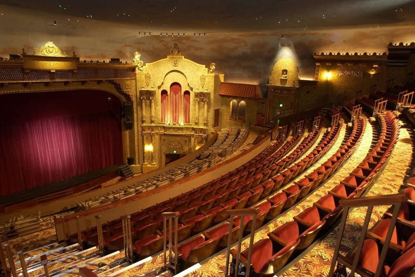Um teatro com palco amplo, arquitetura requintada e fileiras de assentos vermelhos.
