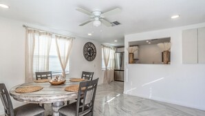 A dining area with a round table, chairs, a ceiling fan, and a kitchen in the background. - Noel Real Estate (Naples)