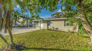 A single-story house with a well-maintained lawn, a driveway, and a tree in the foreground. - Noel Real Estate (Naples)