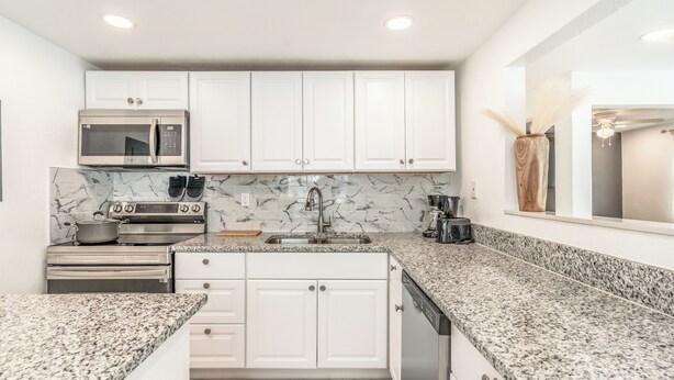 A modern kitchen with white cabinets, a granite countertop, a built-in oven, and a microwave. - Noel Real Estate (Naples)