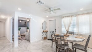 A dining area with a marble floor, a round table with chairs, a ceiling fan, and a view of the outside through large windows. - Noel Real Estate (Naples)